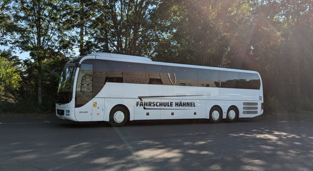 weißer Bus steht vor Bäumen auf einem großen Platz